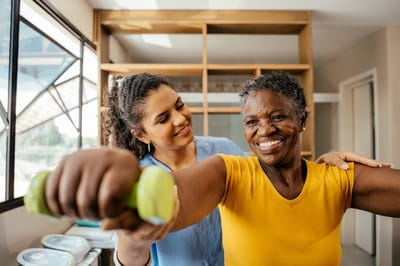 A staff member assisting a resident with weights in a sunny room
