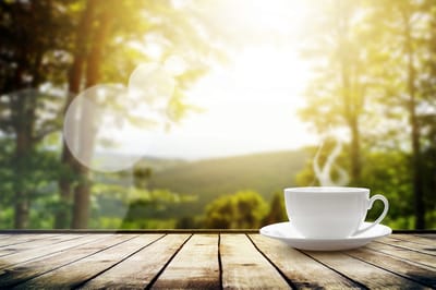 A steaming cup of coffee on a wooden table with a beautiful outdoor background