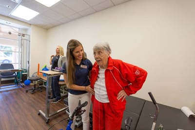 Staff assisting an elderly resident in a therapy setting.
