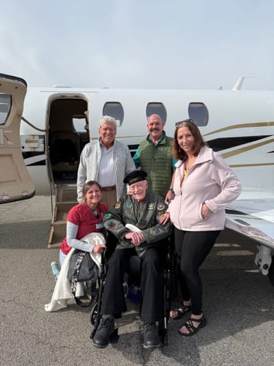 Group of people with a veteran by an aircraft.