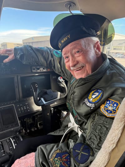 Elderly man in pilot uniform smiling inside cockpit.