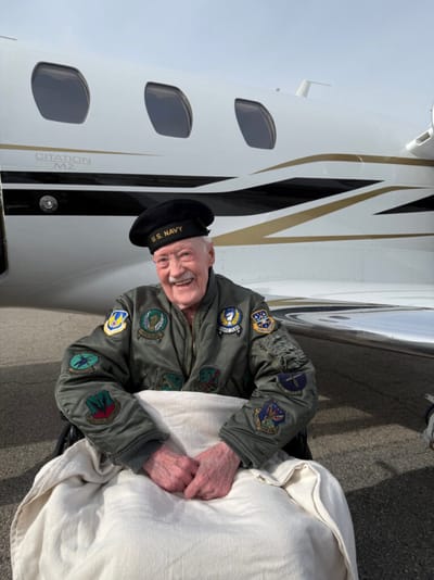 Smiling veteran in military jacket near a private jet
