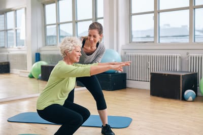 Senior woman exercising with trainer indoors
