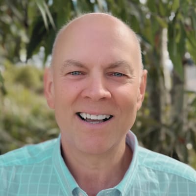 Smiling man outdoors with greenery in background.
