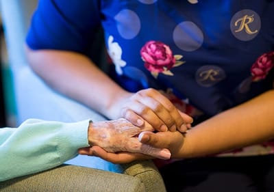 Caregiver holding the hand of a senior resident.