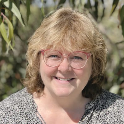 Smiling woman outdoors with greenery in background.