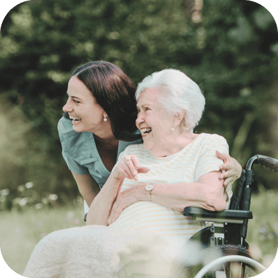 Caregiver and senior resident laughing in a garden.