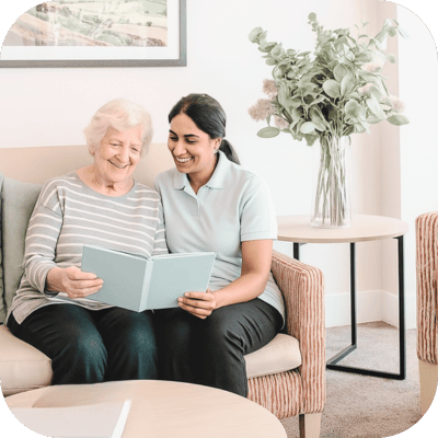Senior resident reading with caregiver in a cozy space.