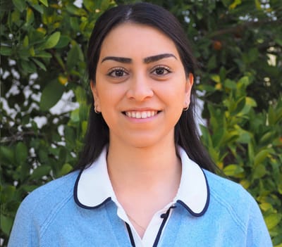 Staff member smiling in front of greenery.