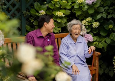 An elderly woman laughing with a staff member outdoors.