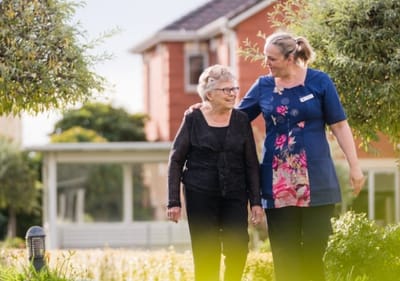 Staff member walking with a resident in the garden.