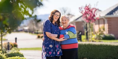 A caregiver and resident smiling outdoors.