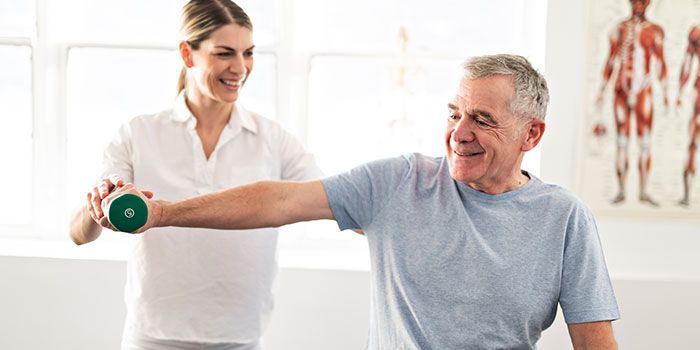 Therapist assisting senior with weights during exercise.