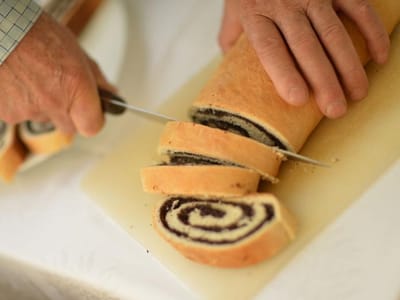 Hands slicing a rolled pastry on a cutting board.