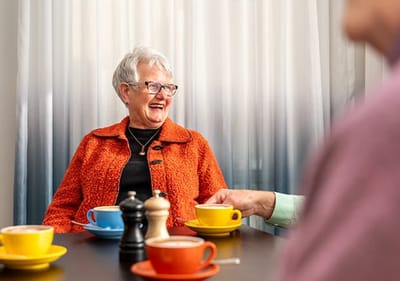 An older woman laughing with coffee cups on the table.