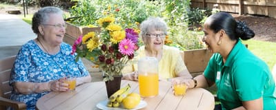 Two residents enjoying drinks with a staff member outdoors.