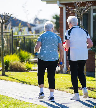 Two elderly women walking outside with weights