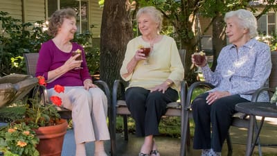 Three residents enjoying drinks outside in a garden area.