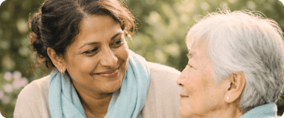 A caregiver smiling at a senior in a garden