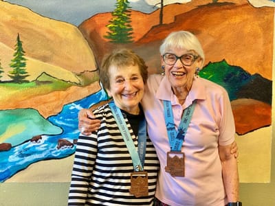 Two smiling residents with medals in front of a mural.