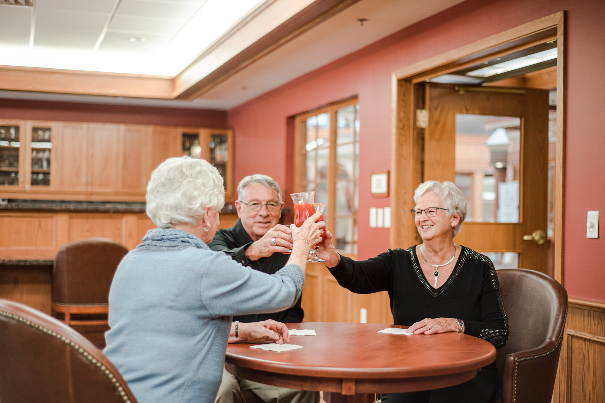 Three seniors enjoy a toast in a common area.