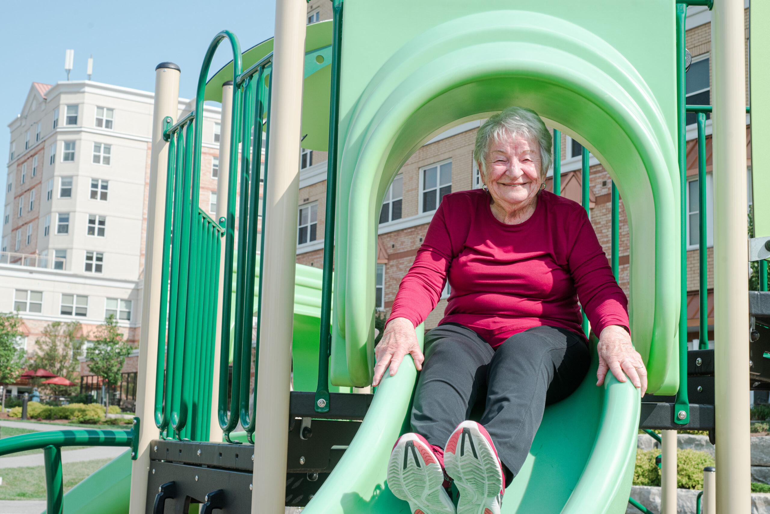 Senior woman joyfully sliding down playground slide.