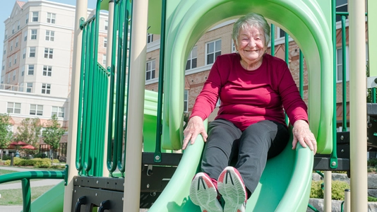 Senior woman enjoying a slide at an outdoor playground.
