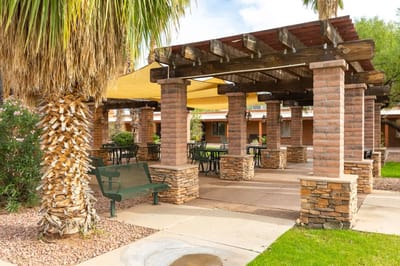 Outdoor shaded seating area with stone columns and palm trees