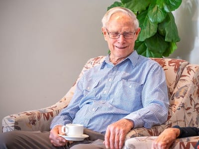 Smiling elderly man holding a coffee cup in a cozy chair