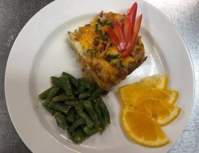 Plate of food with cheese casserole, green beans, and orange slices