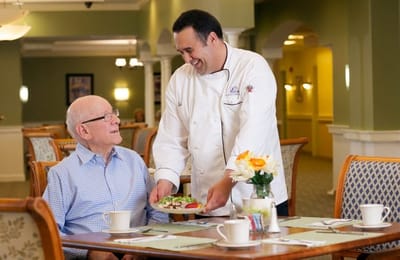 Chef serving a meal to a resident in the dining area