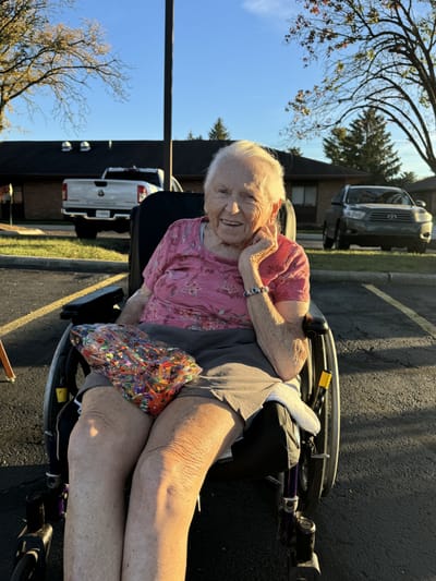 An elderly woman sitting in a wheelchair outdoors.