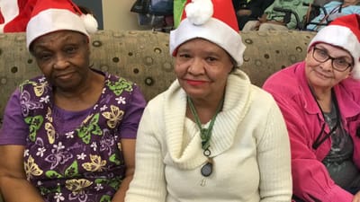 Three residents wearing Santa hats in a common area