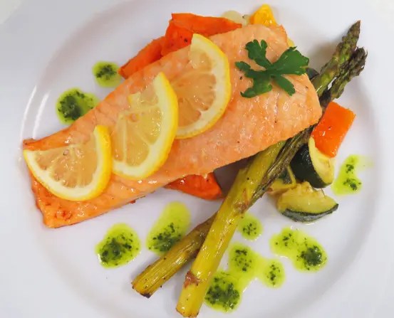 A plate of salmon with vegetables and lemon slices