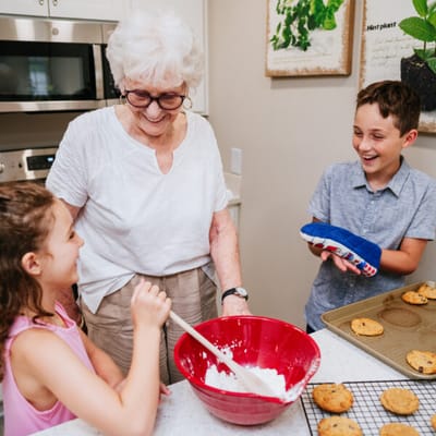 An elderly woman baking cookies with two children