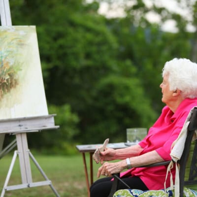 Senior resident painting outdoors in a serene setting