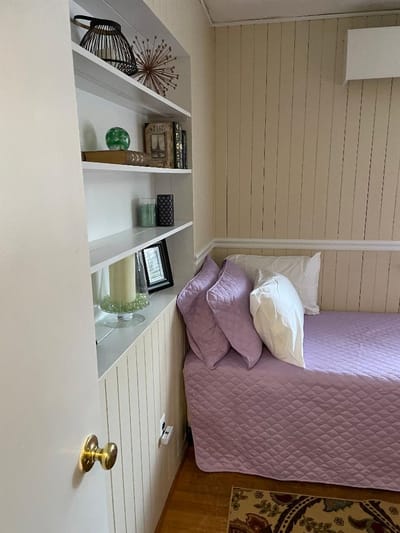 A cozy bedroom with a lavender bedspread and shelves