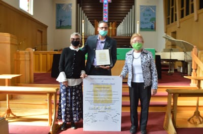 Three people holding a certificate in a church interior.