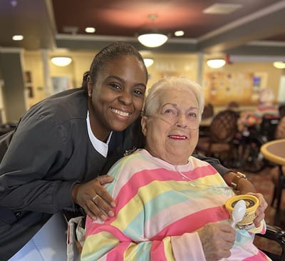 Senior resident enjoying ice cream with staff member in a common area