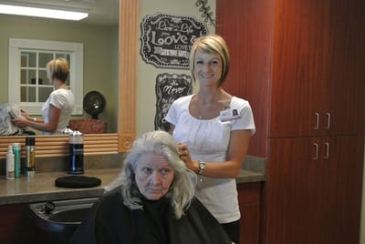 A staff member styling a resident's hair in a salon setting