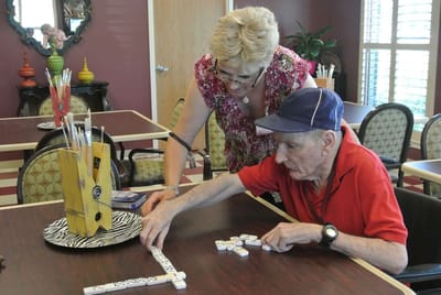 Resident playing dominoes with staff assistance