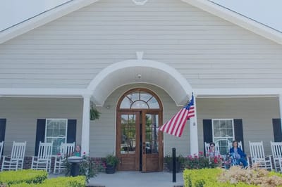 Front entrance of Arcadian Cove Senior Living with rocking chairs and flag