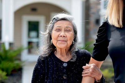 A smiling senior woman standing outdoors with staff assistance