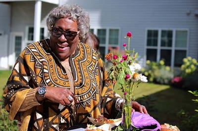 Resident smiling outdoors, enjoying a meal with flowers
