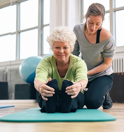 Senior woman stretching assisted by a staff member