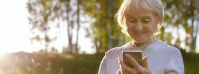 Senior woman smiling while using a smartphone outdoors.