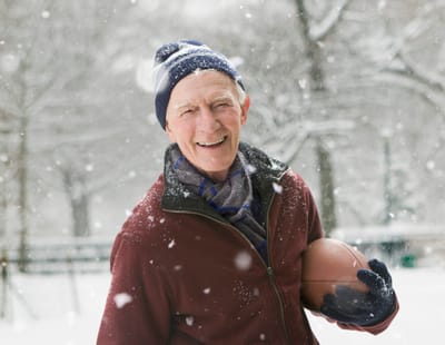 Senior man smiling with a football in the snow.