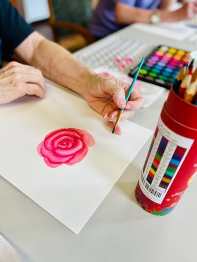 A person painting a pink rose with watercolors.