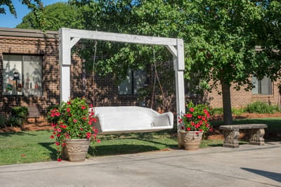 Outdoor swing surrounded by flowers in a garden area.