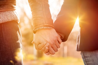 Two hands holding in an outdoor setting.